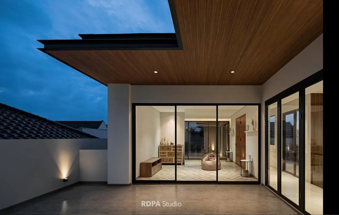 Terrace at dusk under a timber soffit, bedroom lit behind the glass